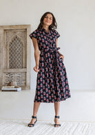 Woman wearing Black floral midi shirt dress with cap sleeves and tie waist. 