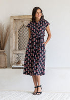 Woman posing in a 100% cotton Black floral midi shirt dress with cap sleeves and tie waist. 