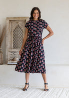 Woman wearing a 100% cotton black floral print midi dress with short sleeves and tie waist. 