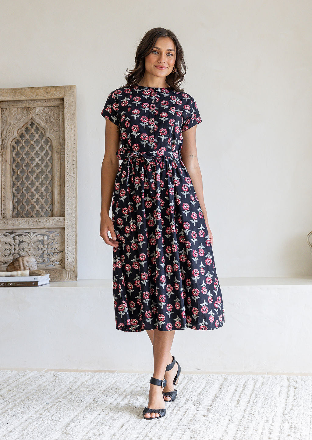 Woman poses in a pure cotton black floral print midi dress with short sleeves and gathered waist. 