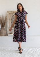 Woman posing in a 100% cotton Black floral midi shirt dress with cap sleeves and tie waist. 