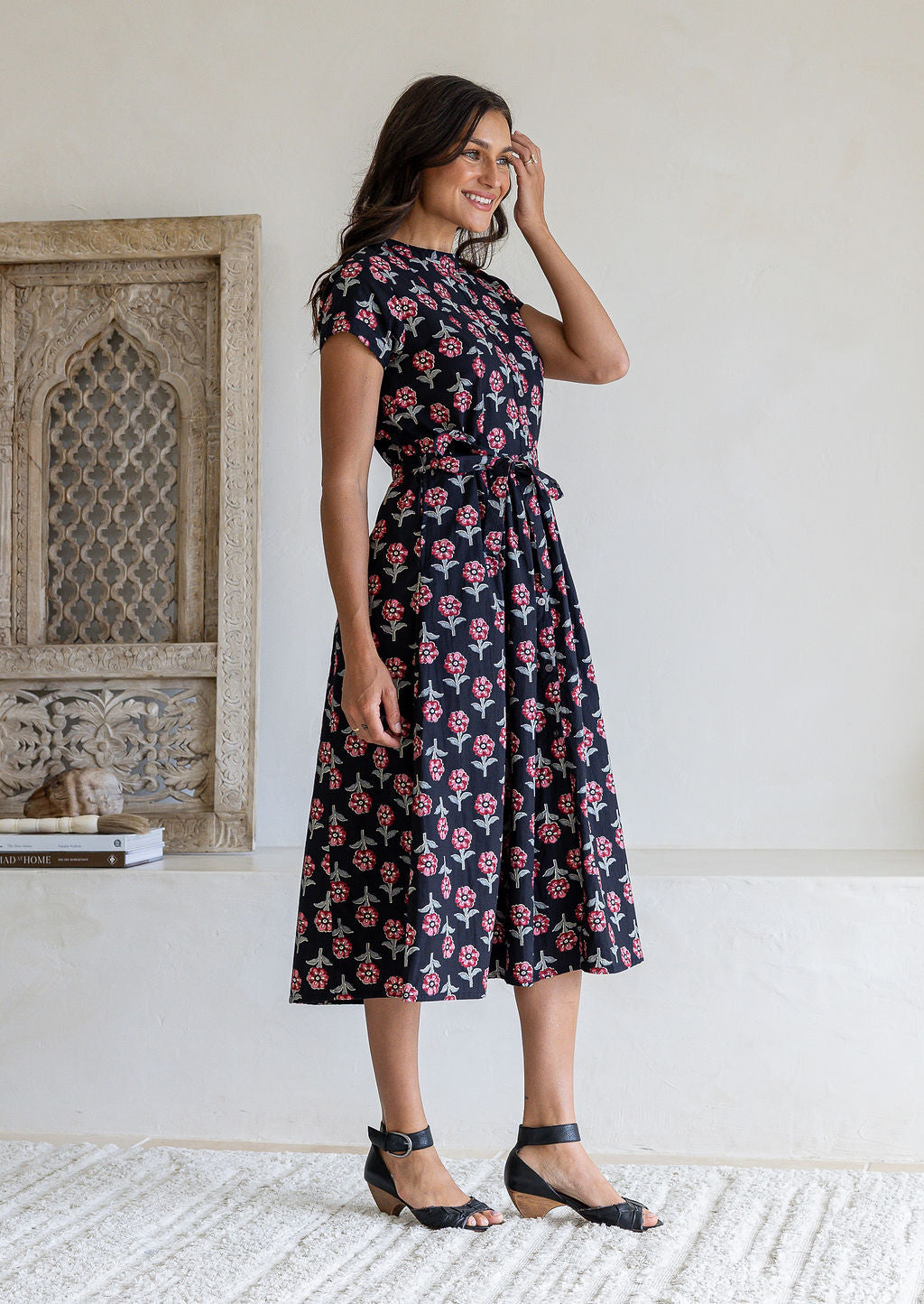 Model standing sideways wearing a black midi dress with floral print, short sleeves and tie waist. 