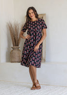 Woman poses in a black based cotton floral short sleeve dress with round neckline