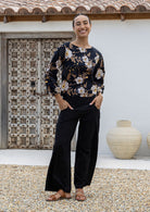 Woman wearing a 100% cotton black based floral print top and plain black pants in an outdoor setting