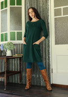 Woman wearing green corduroy A-line tunic dress with 3/4 sleeves with hands in pockets 