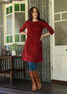 Woman in a red dress and brown boots standing in a room with patterned wallpaper.