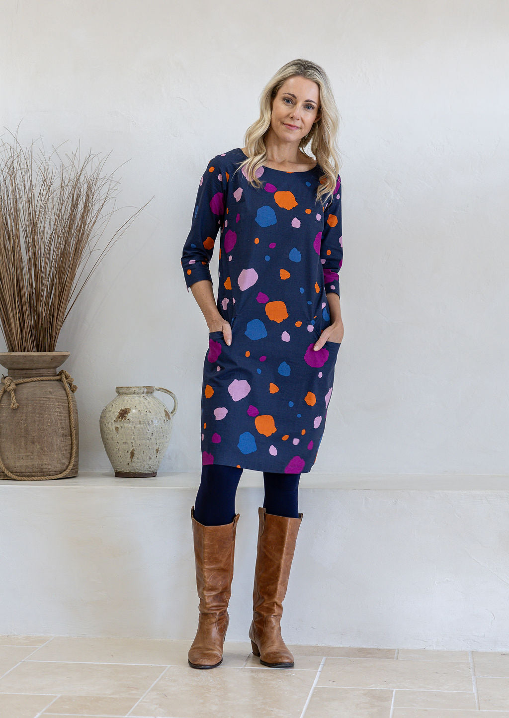 Model wears 3/4 sleeved cotton dress in colourful bold print with both hand in pockets