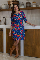 A woman wearing a 100% cotton knee-length dress in navy based floral print with 3/4 sleeves and round neckline.