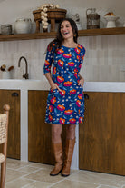 A woman wearing a 100% cotton knee-length dress in navy based floral print with 3/4 sleeves and both hand in pockets