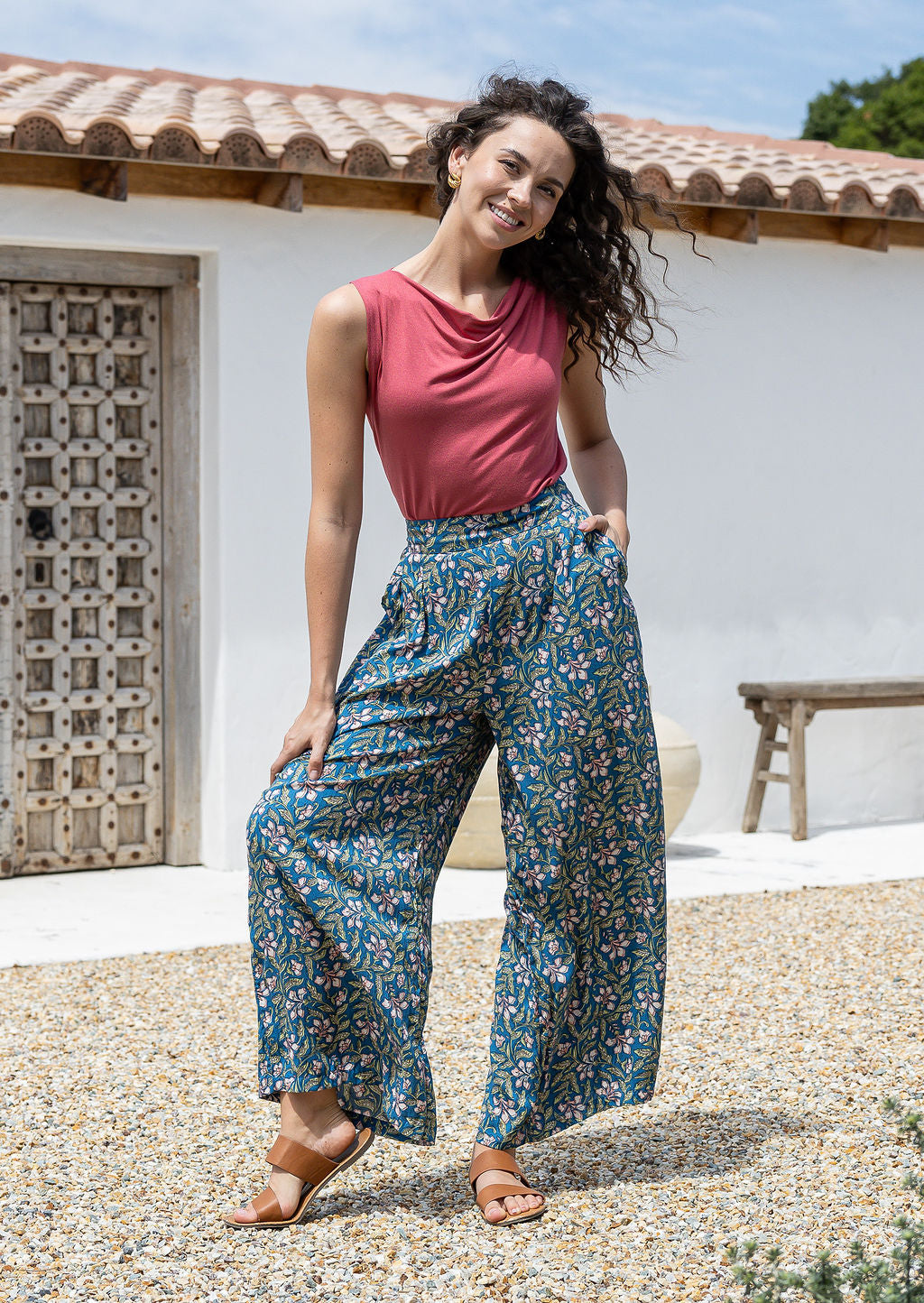 woman wearing wide legged blue based floral print 100% rayon pants and wide neck mod top with hand in pocket
