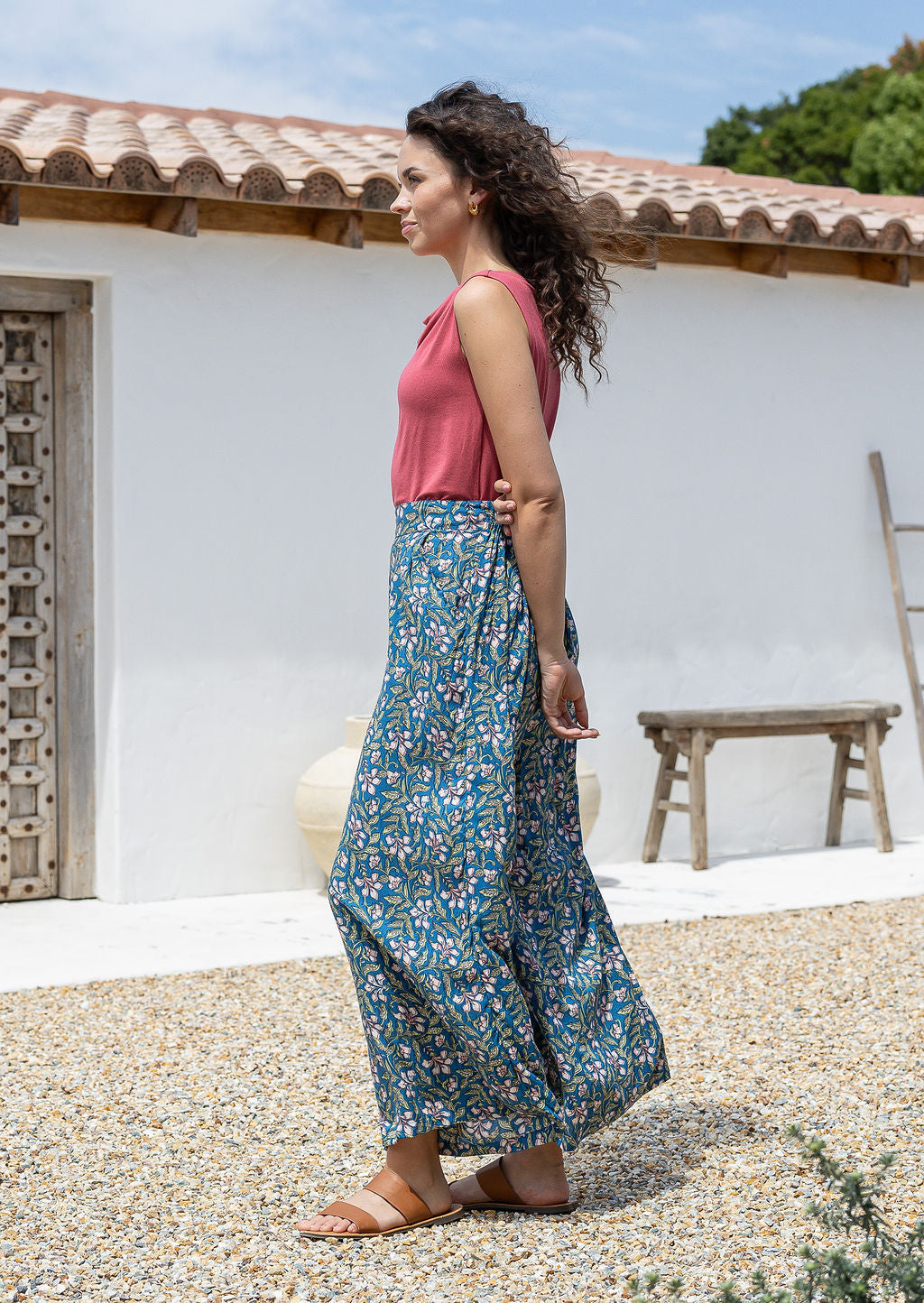 woman stands sideways wearing a wide legged rayon pants with blue based pink and white floral print.