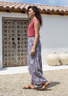 Woman in a pink top and blue based floral pants standing in front of a rustic door and white wall.