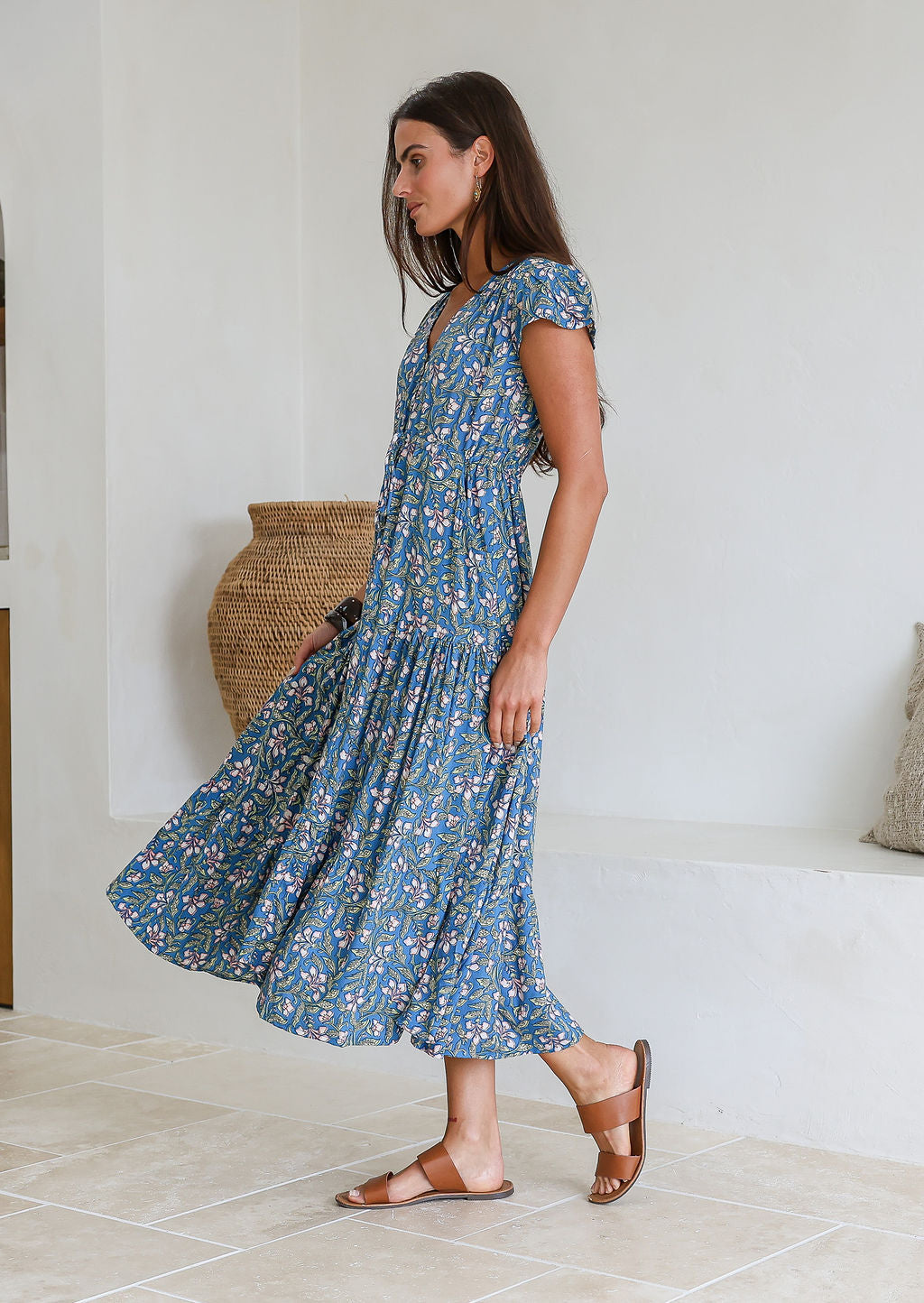 Woman stands sideways wearing a rayon maxi dress with voluminous tiered skirt and buttoned bodice