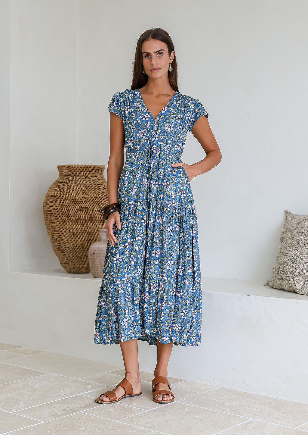 Woman stands with one hand in pocket of a rayon maxi dress with tulip sleeves, V-neckline and buttoned bodice