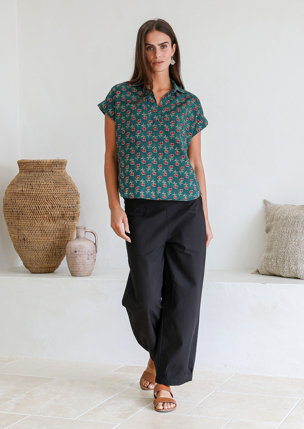 Woman wearing a green based relaxed fit, shirt style floral cotton top with black plain pants.