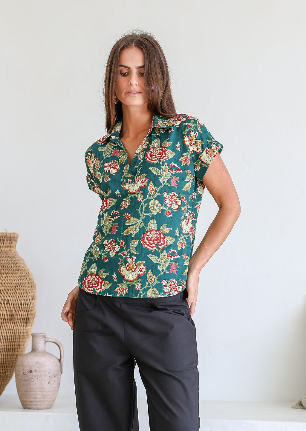 Woman wearing a green based relaxed fit, shirt style floral cotton top with black cotton pants.