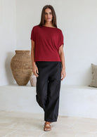 Woman wearing a maroon stretch rayon short sleeved batwing top and black pants standing in a room with decorative vases.