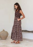 Woman wearing a Indian patterned cotton dress standing in a minimalistic room with her hands in her pockets 