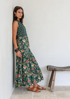 Model leans on wall wearing a beautiful floral printed cotton maxi dress with buttoned bodice, 3/4 sleeves and V neckline.