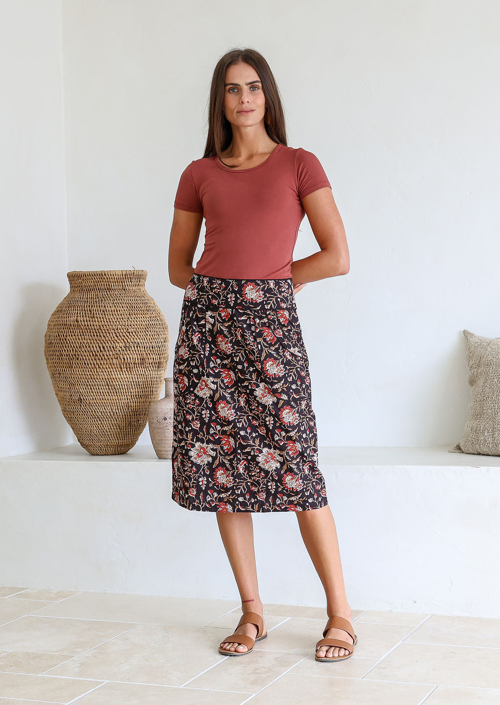 Woman wearing a high-waisted, knee length pencil skirt with piped detailing and pockets in a black based floral print.