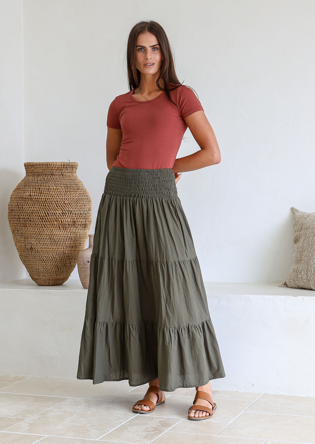 woman wearing a simple pink top and 100% cotton maxi skirt in olive green shade in a room with decorative vases.