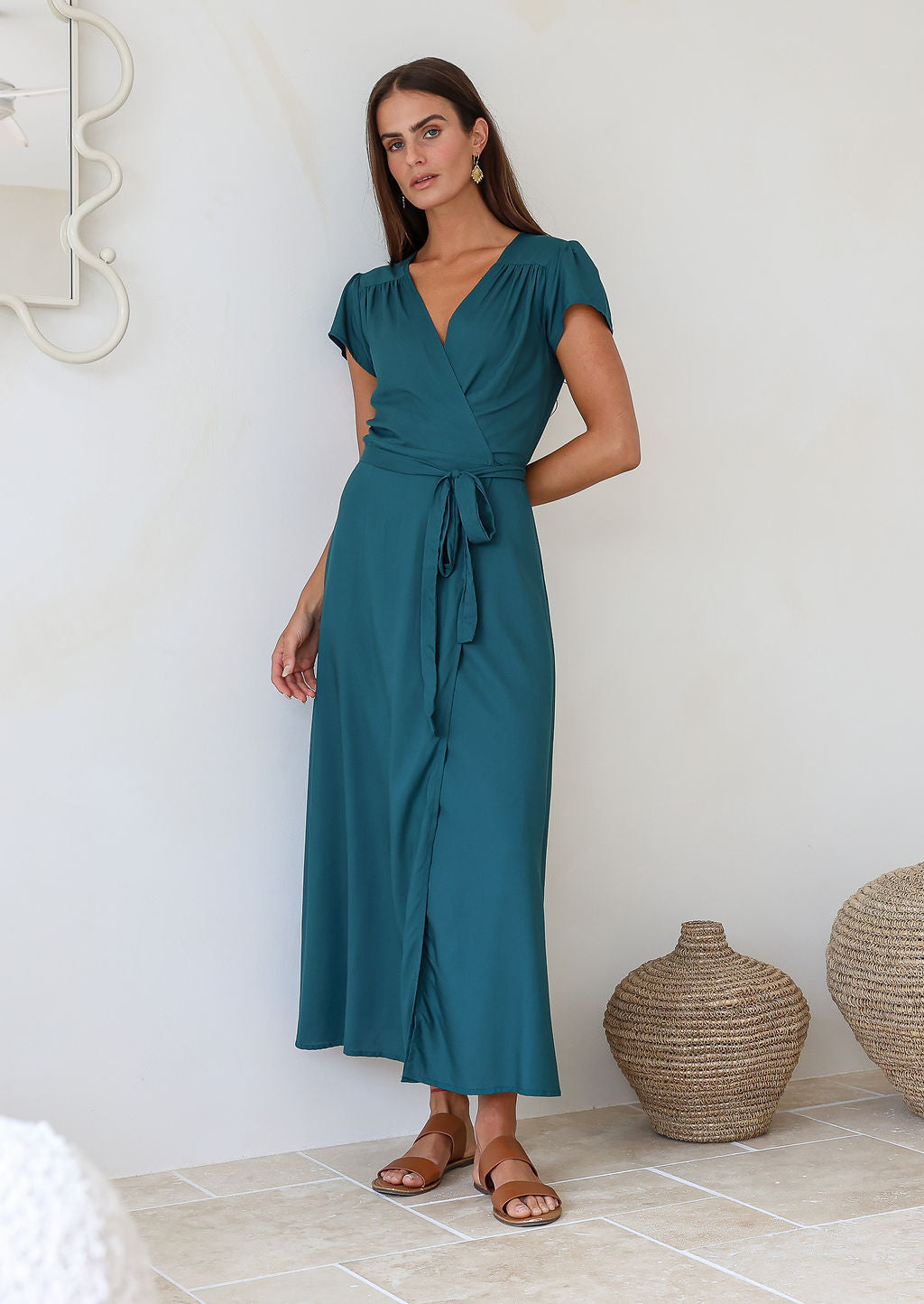 Woman wearing a teal rayon wrap long dress standing in a room with decorative vases.
