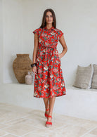 Woman wearing a shirt style cotton midi length dress with buttoned bodice, pockets, collar and cap sleeves