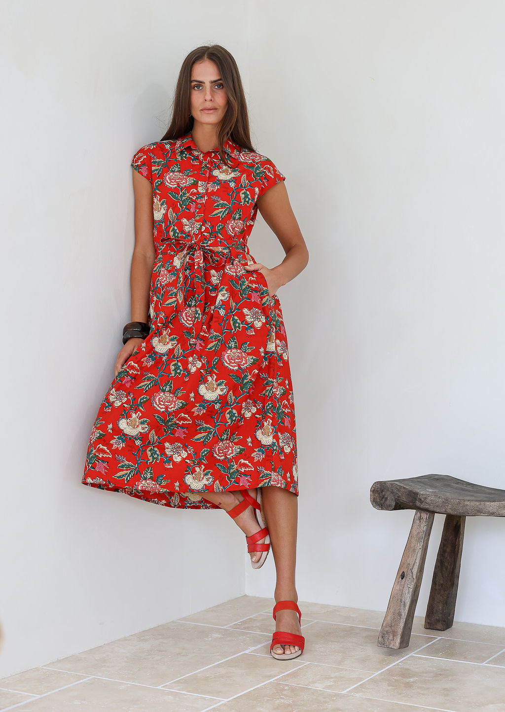 Woman wearing a shirt style cotton midi length dress with buttoned bodice, pockets, collar and cap sleeves