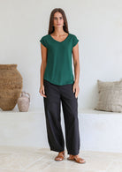 Woman wearing a 100% rayon forest green V-neck T-shirt and black pants, standing against a wall.