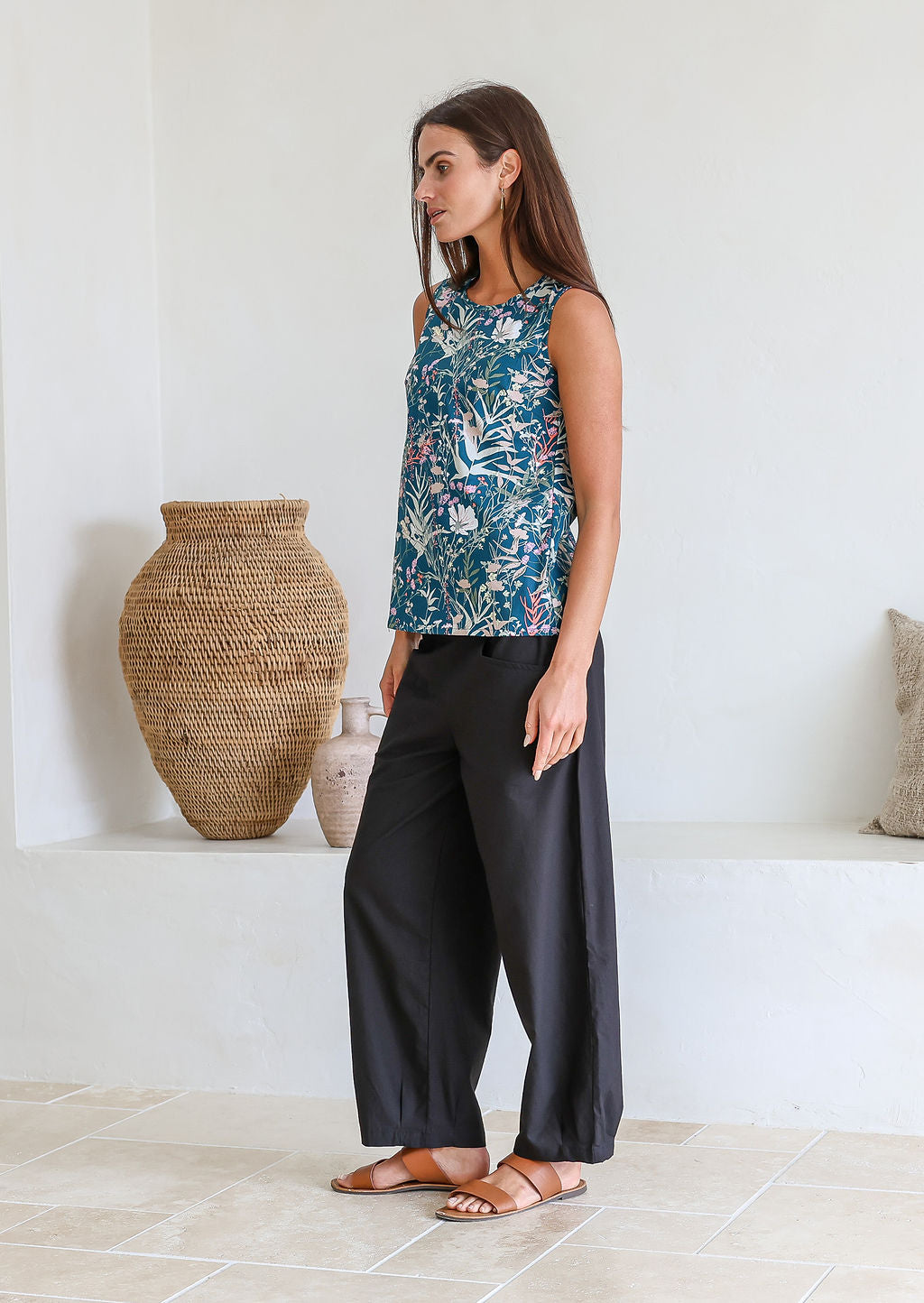 Woman standing sideways wearing a 100% cotton retro floral top, sleeveless design with side bust darts