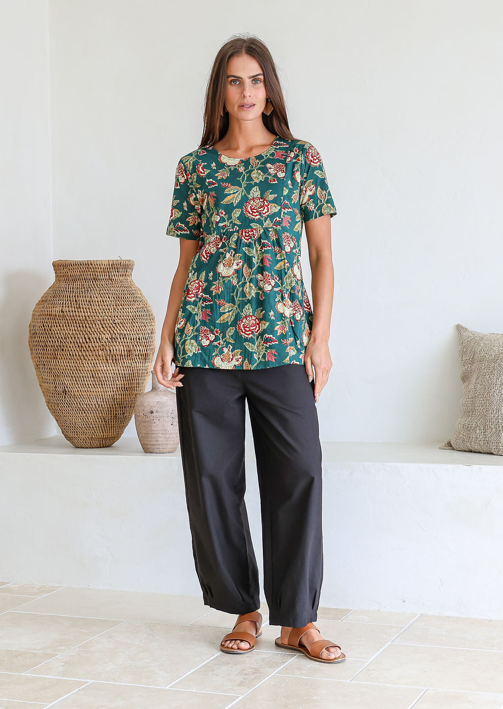 Woman wearing a bottle green based floral print top with short sleeves and an empire waistline, with deep pockets