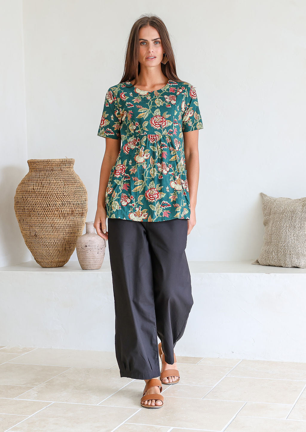 Woman wearing a relaxed fit 100% cotton top in a bottle green based floral print with short sleeves, pockets and gathers under the bust