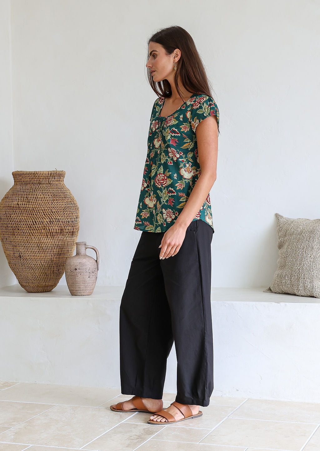 Woman standing sideways wears 100 percent cotton top with short cap sleeves and longer back hem.