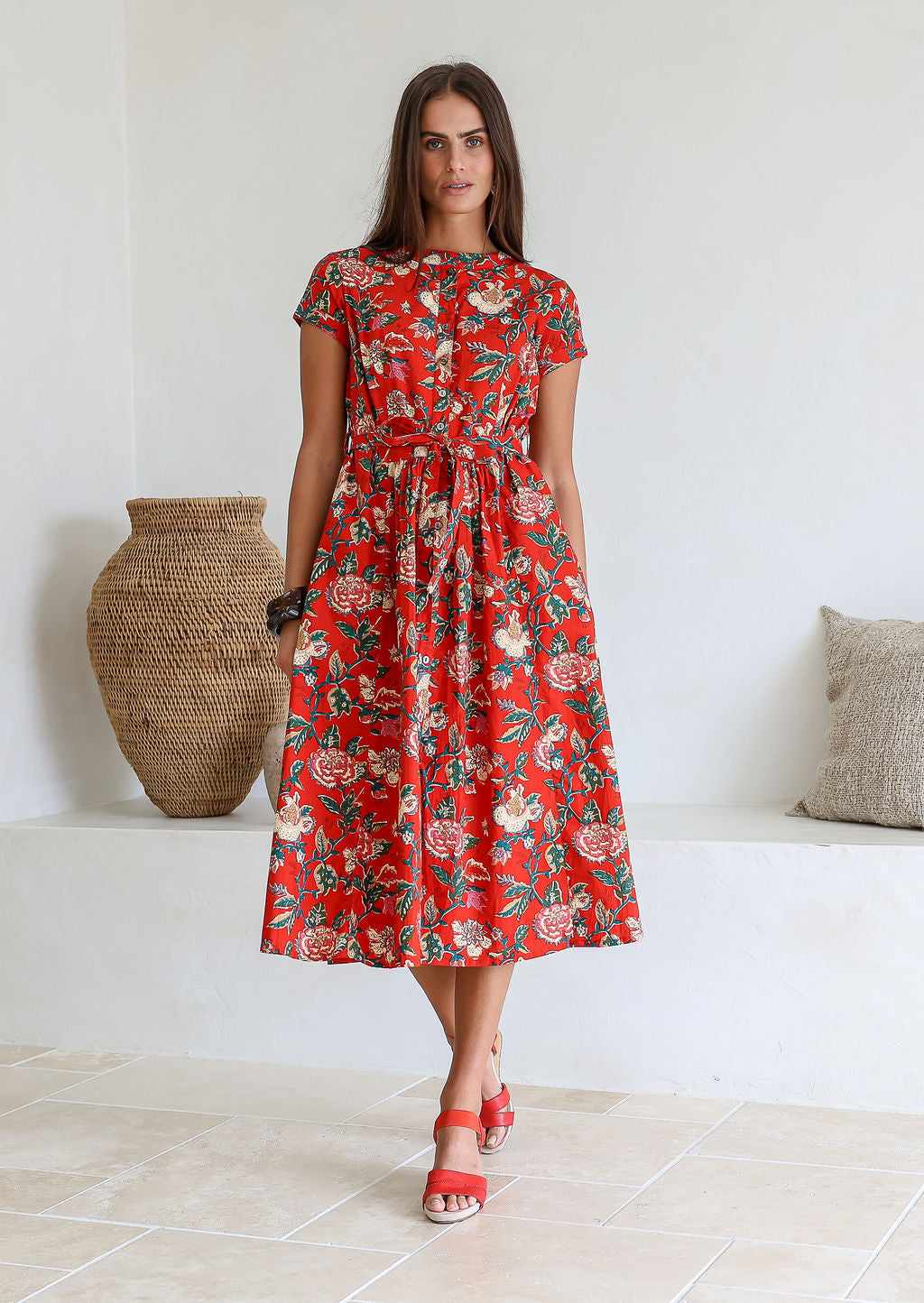 Woman wears retro style cotton button through midi length dress with high round neckline, short sleeves and a removable waist tie.