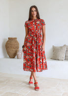 Woman poses in 1950's style short sleeved, button through cotton dress with high round neckline in red based floral print.
