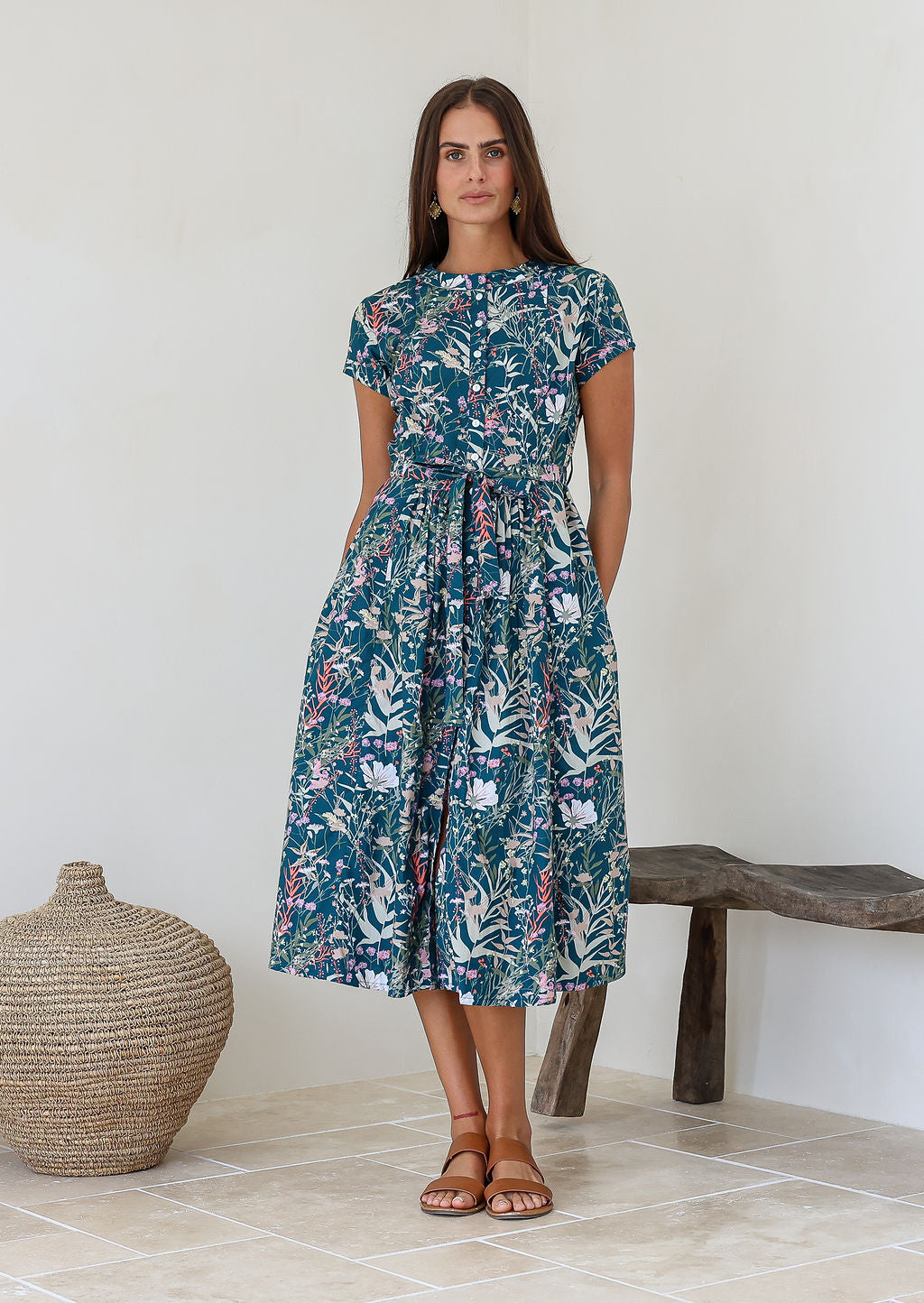 Woman wears retro style cotton button through midi length dress with high round neckline, short sleeves and a removable waist tie.