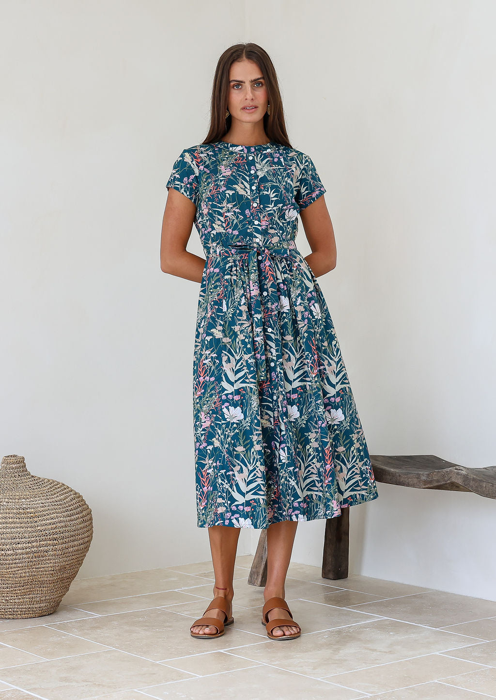 Woman poses in 1950's style short sleeved, button through cotton dress with high round neckline in teal based floral print.