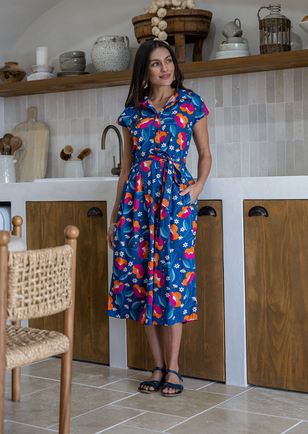 Woman wearing a midi length navy based floral cotton dress with buttoned bodice and one hand in pocket