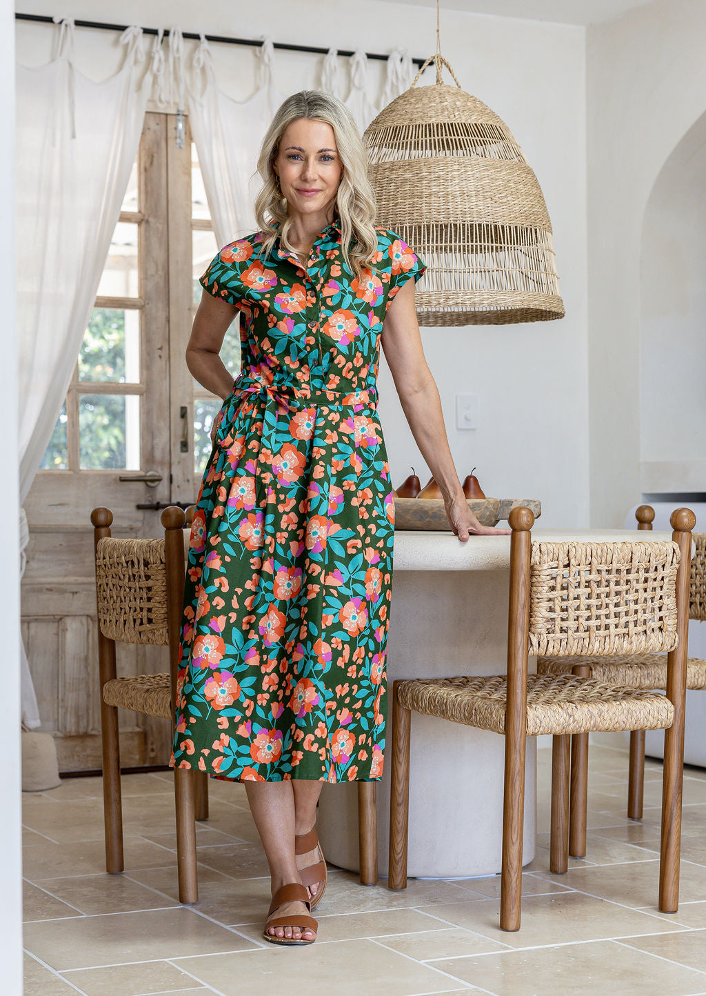 Model stands with wearing a midi length floral printed shirt style cotton dress with cap sleeves, buttoned bodice. 