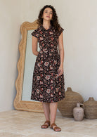 Woman wearing a shirt style cotton midi length dress with buttoned bodice, pockets, collar and cap sleeves