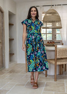 A woman modelling a cap-sleeve cotton midi dress with collar and buttoned bodice, in a vibrant multicolour floral and peacock print
