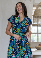Close up of woman wearing a navy blue based peacock print cotton dress with collar, buttoned bodice and waist tie