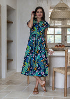 Woman wearing a peacock print cotton midi length dress with a collar, buttoned bodice and waist tie