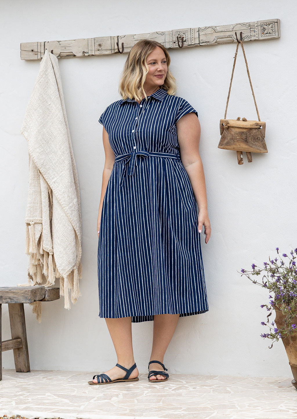 Woman wearing a midi length navy based white stripes print cotton dress with buttoned bodice 
