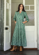 Woman poses in sage green based floral cotton maxi dress with buttoned bodice, 3/4 sleeves and flowy three tiered maxi skirt