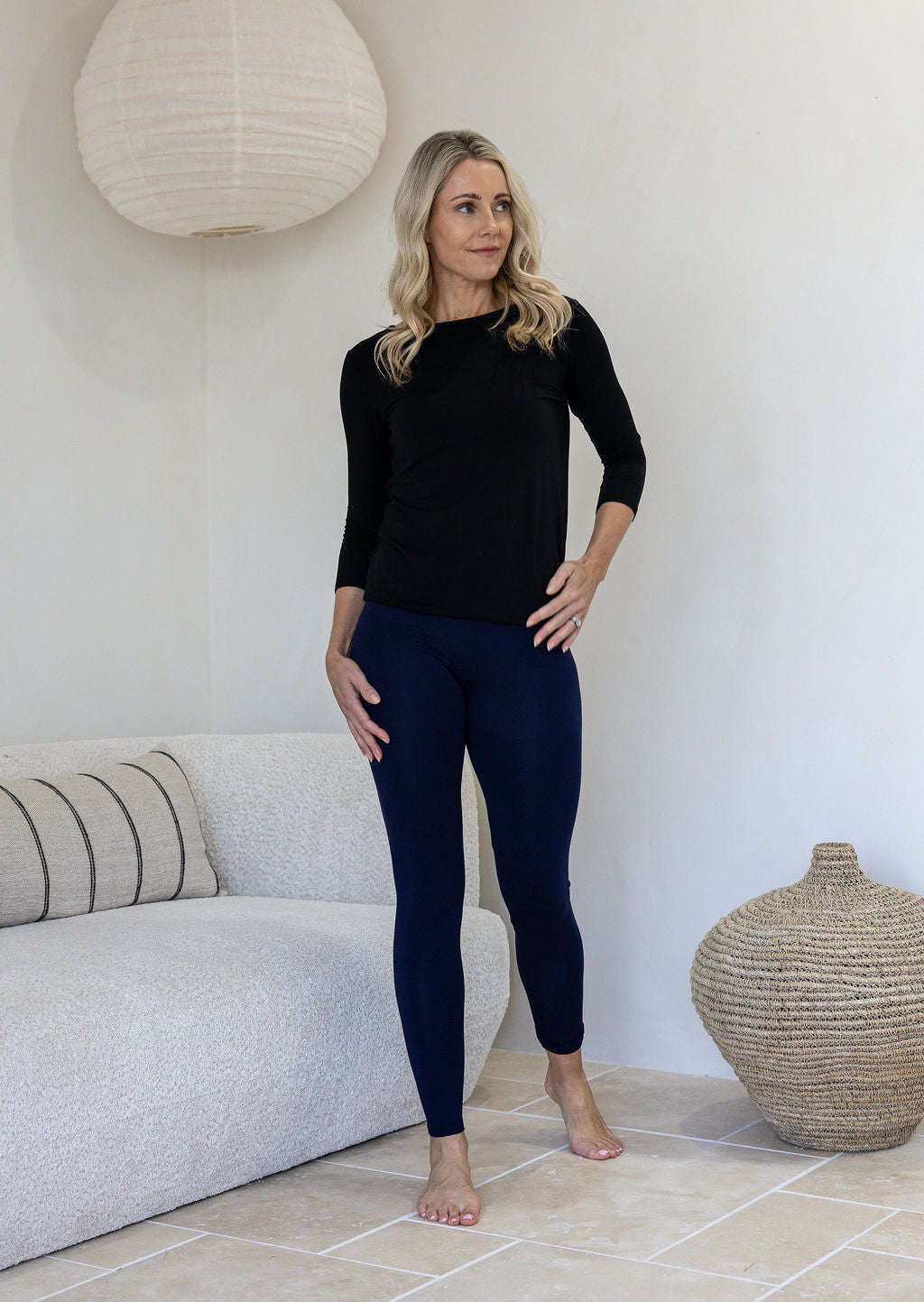 Woman wearing a 100% rayon jersey soft stretch leggings in navy blue standing in a minimalistic room. 