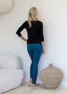 Woman standing backwards wearing high waisted full length soft rayon leggings in teal blue