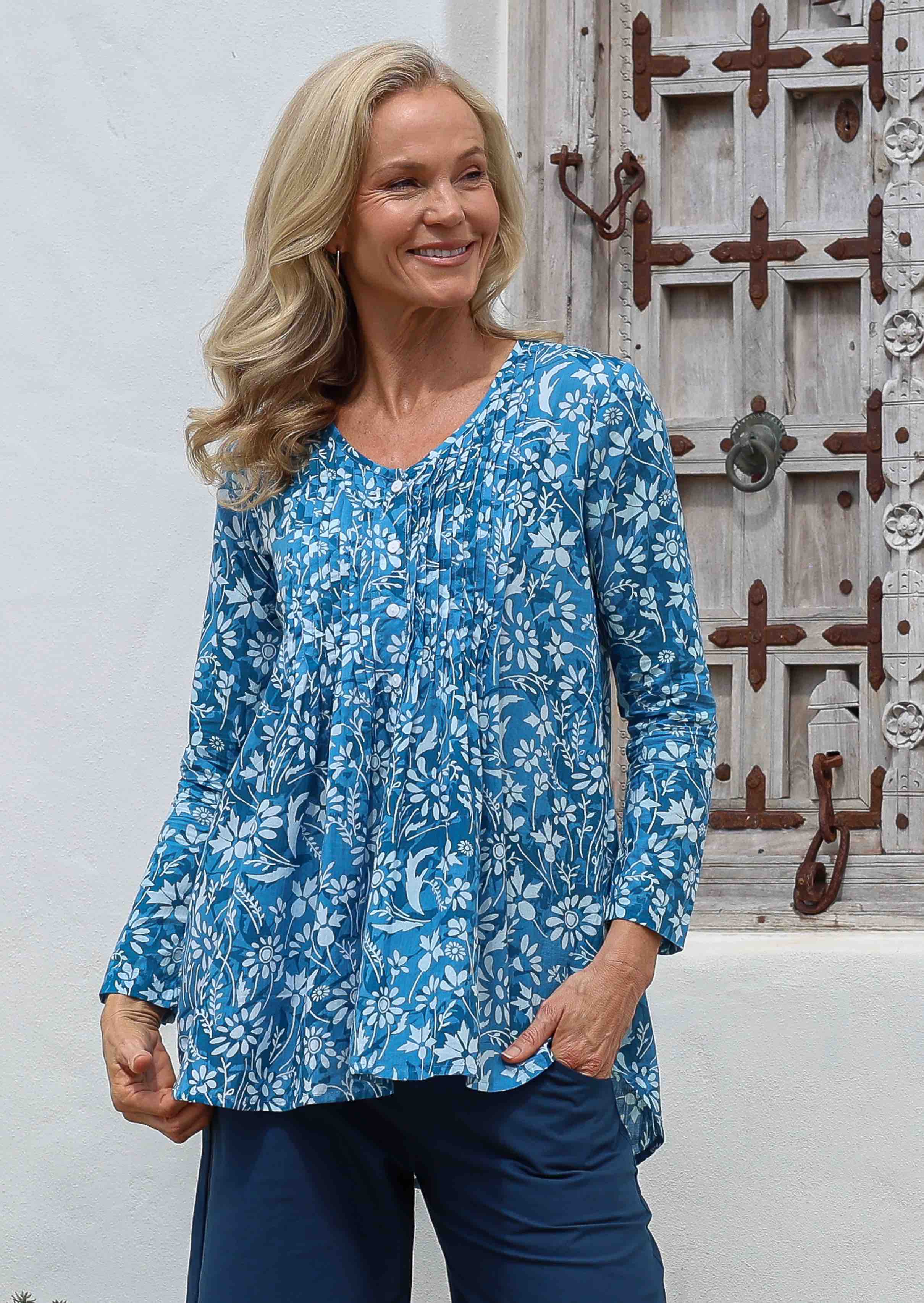 Woman wearing a blue floral relaxed fit a-line cotton blouse with V neckline, long sleeves, button through front and small pleats at front and back.