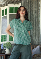 Woman wearing a sage green based relaxed fit, shirt style floral cotton top with plain pants.