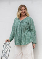 Woman wearing a sage green based cotton floral long sleeve relaxed fit blouse with a V-neckline.